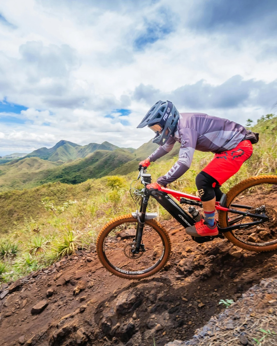 A mountain biker riding a rocky trail above green mountain valleys